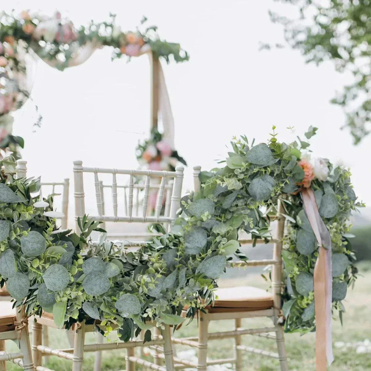 Decorative floral arch and chair with greenery and ribbons in an outdoor setting