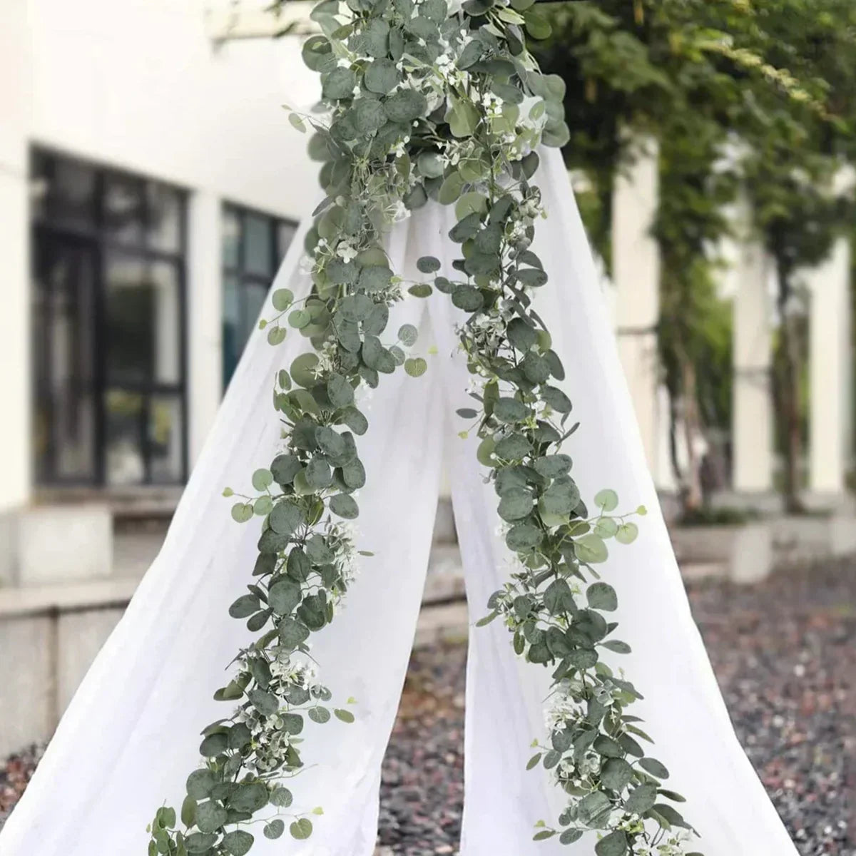 Decorative arch with greenery and white fabric in an outdoor setting