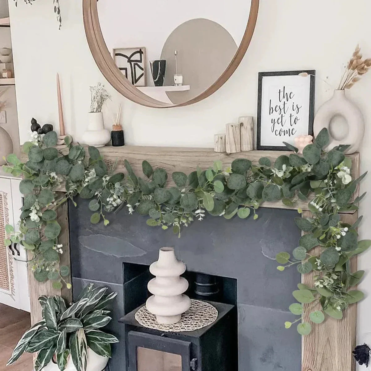 Decorative greenery on a fireplace mantel with a mirror and framed picture in the background.