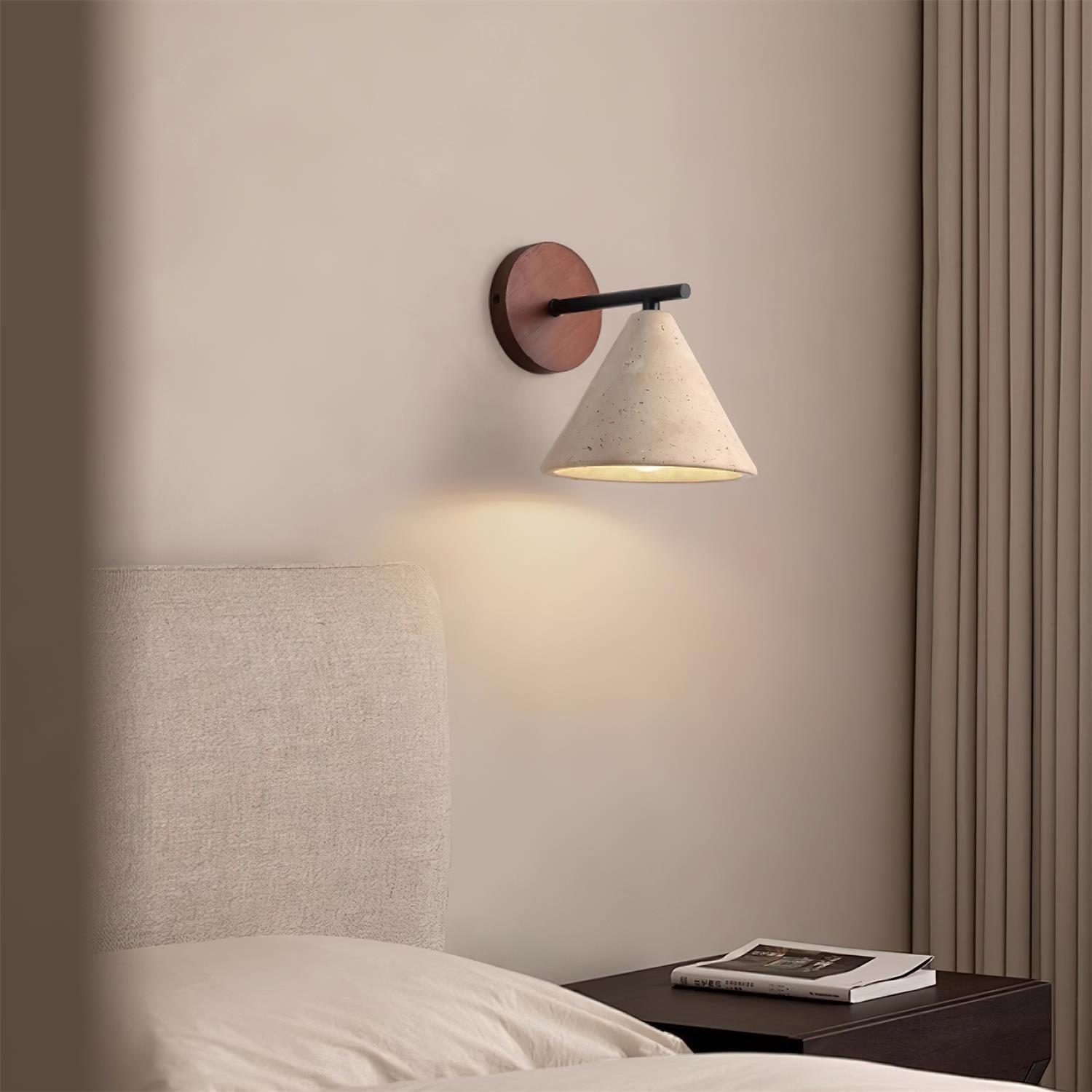 Wall-mounted lamp on a neutral wall above a bed with a side table.
