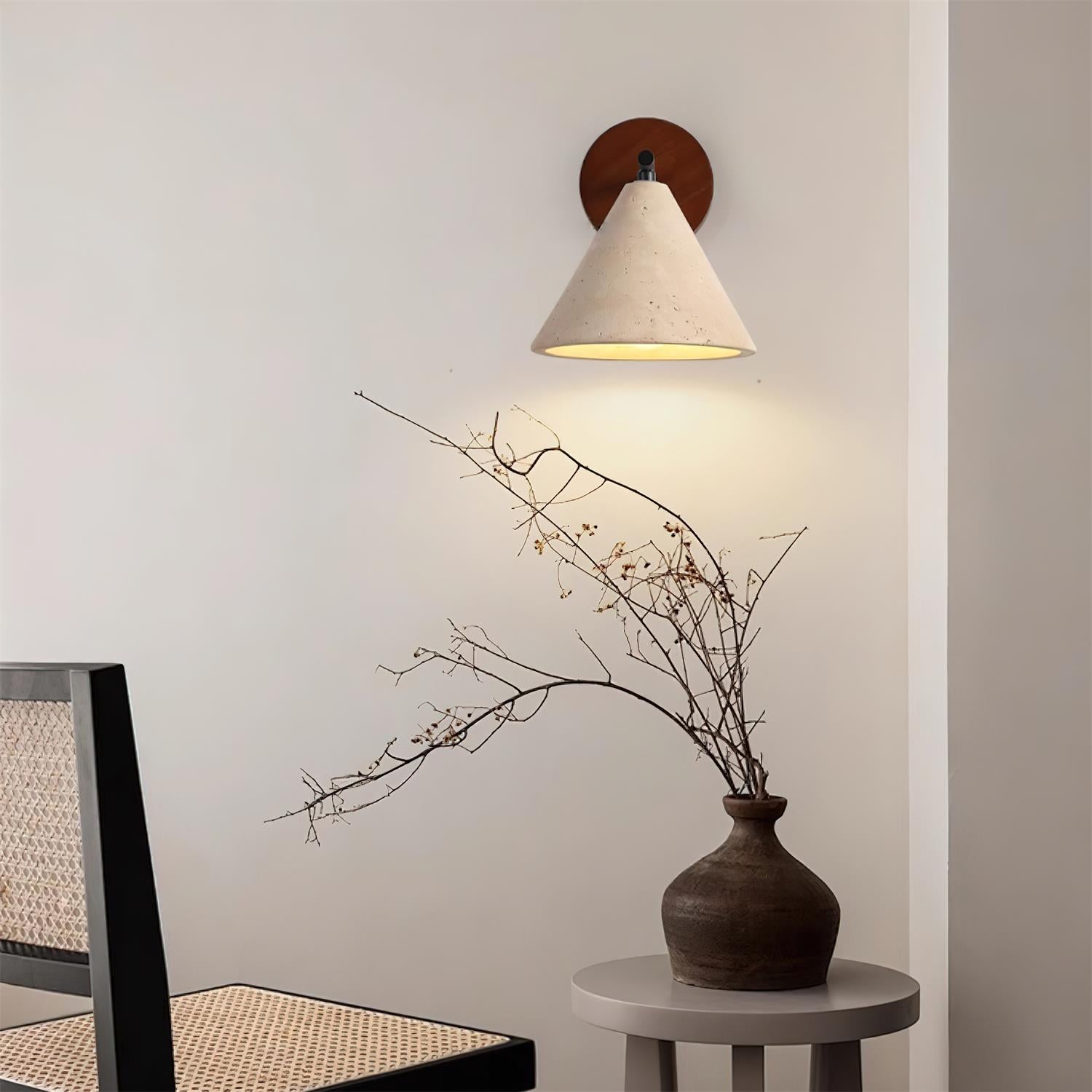 Wall-mounted light fixture casting a warm glow on a branch and vase against a neutral wall.