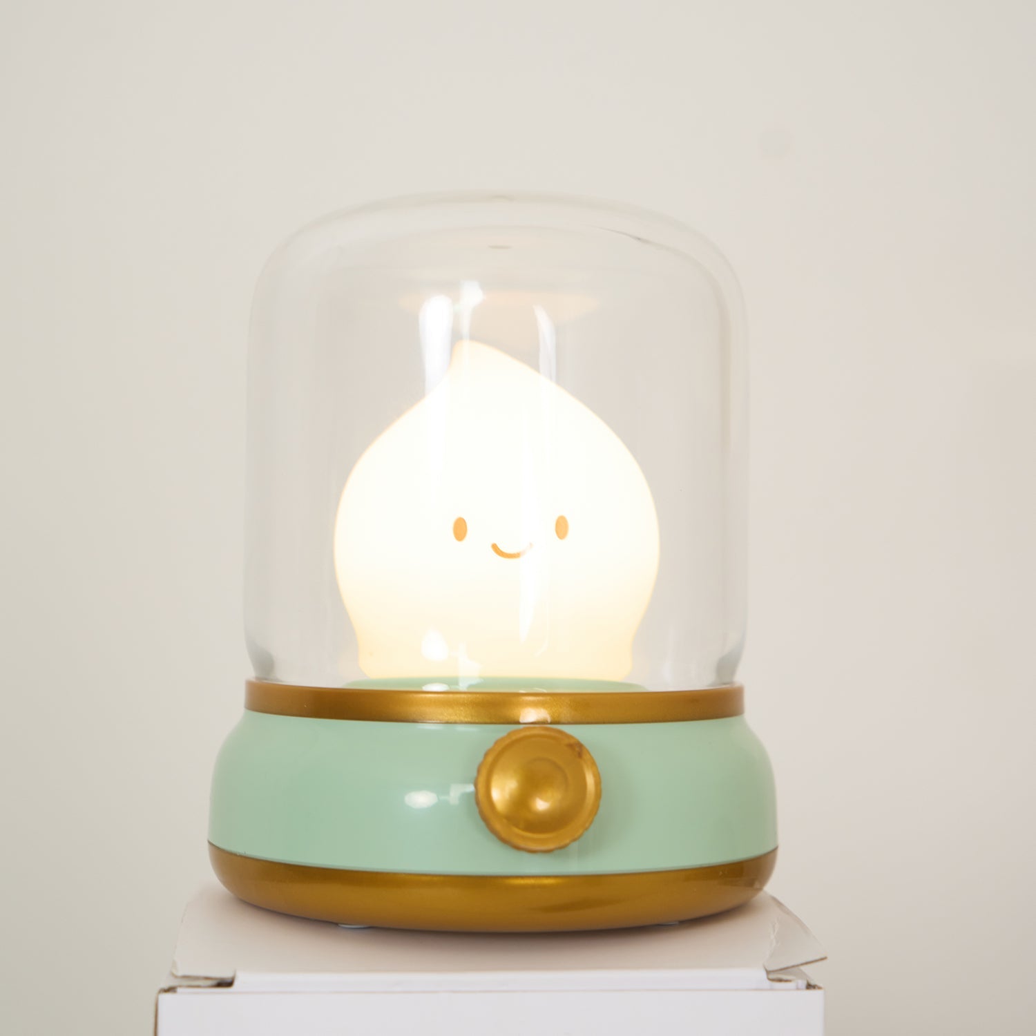 Cute lamp with a smiling face inside a glass dome on a white surface.