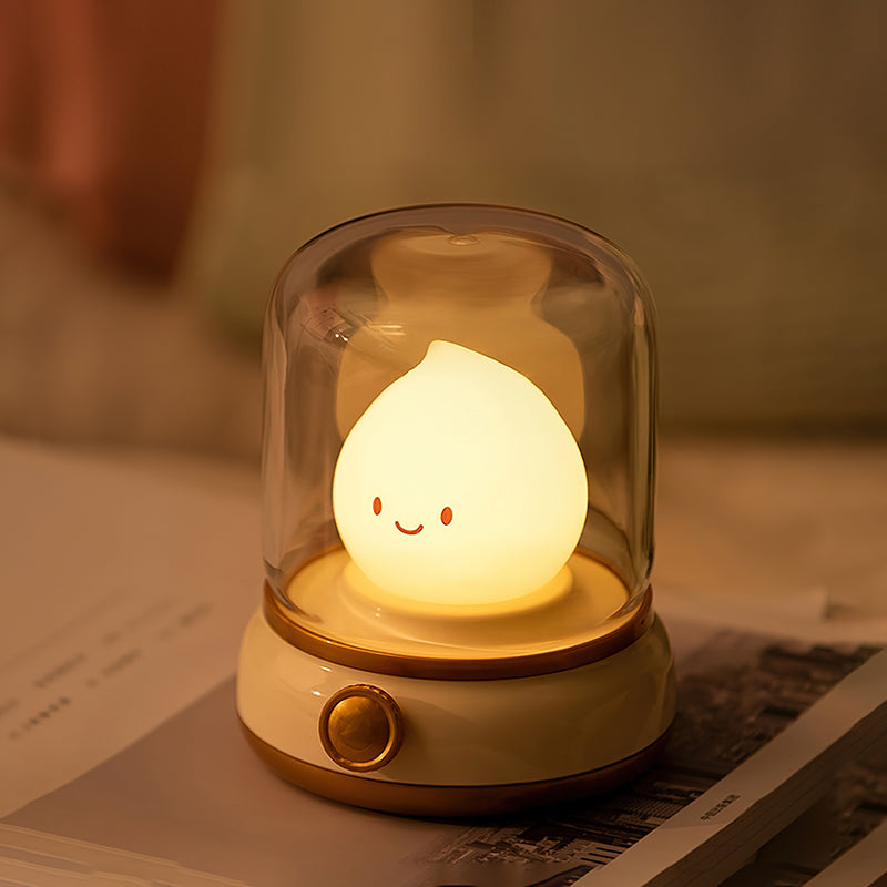 Cute lamp with a smiling face inside a glass dome on a surface.
