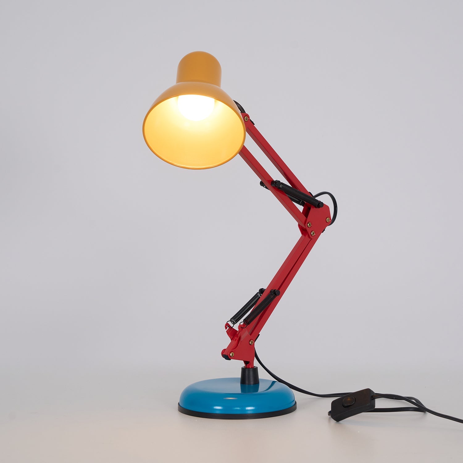 Colorful desk lamp with a yellow shade, red arm, and blue base on a light gray background.