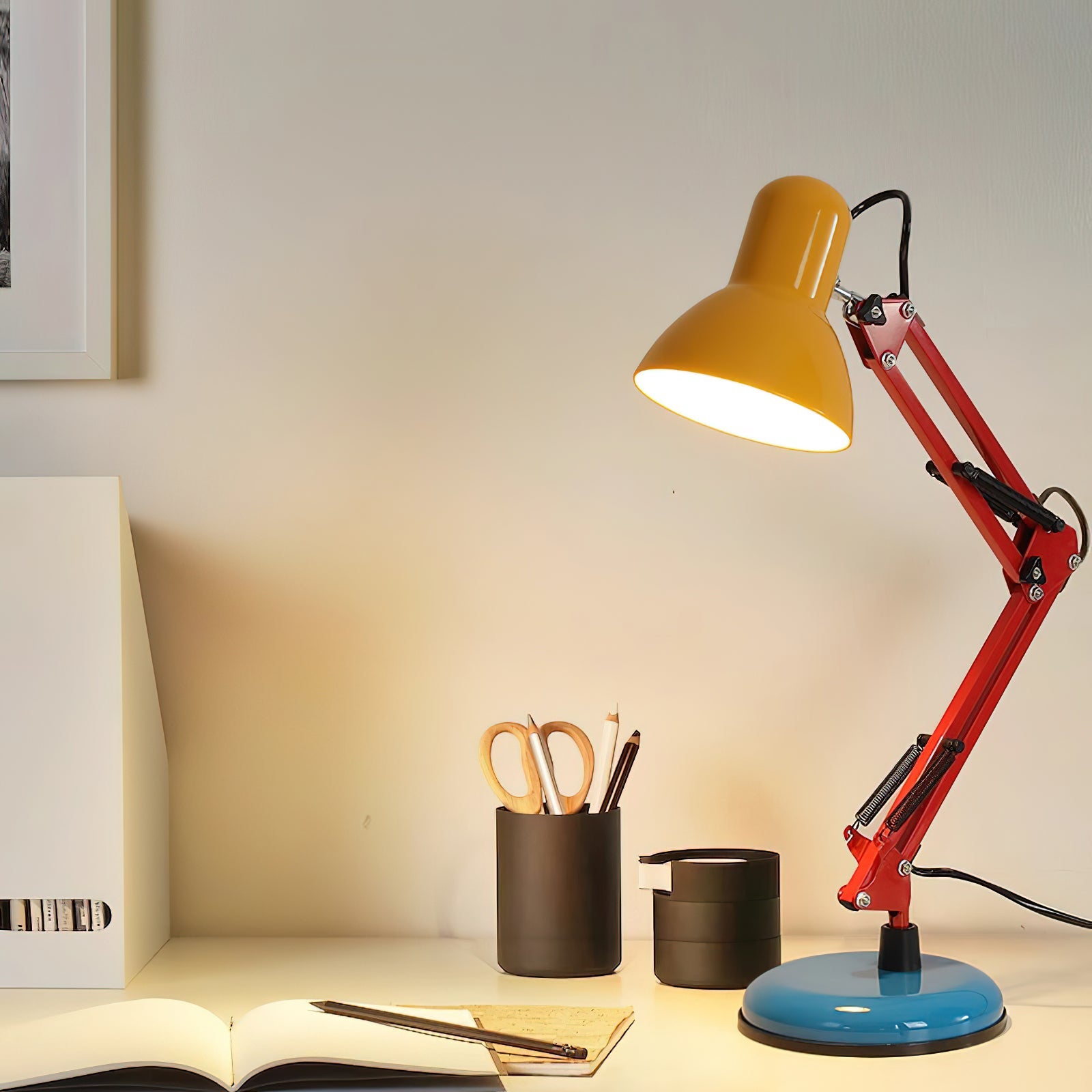 Desk lamp with yellow shade and red arm on a desk with stationery items.