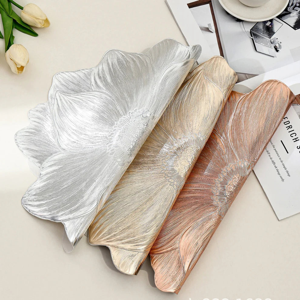 Three decorative leaf-shaped platters in silver, gold, and rose gold on a light surface.