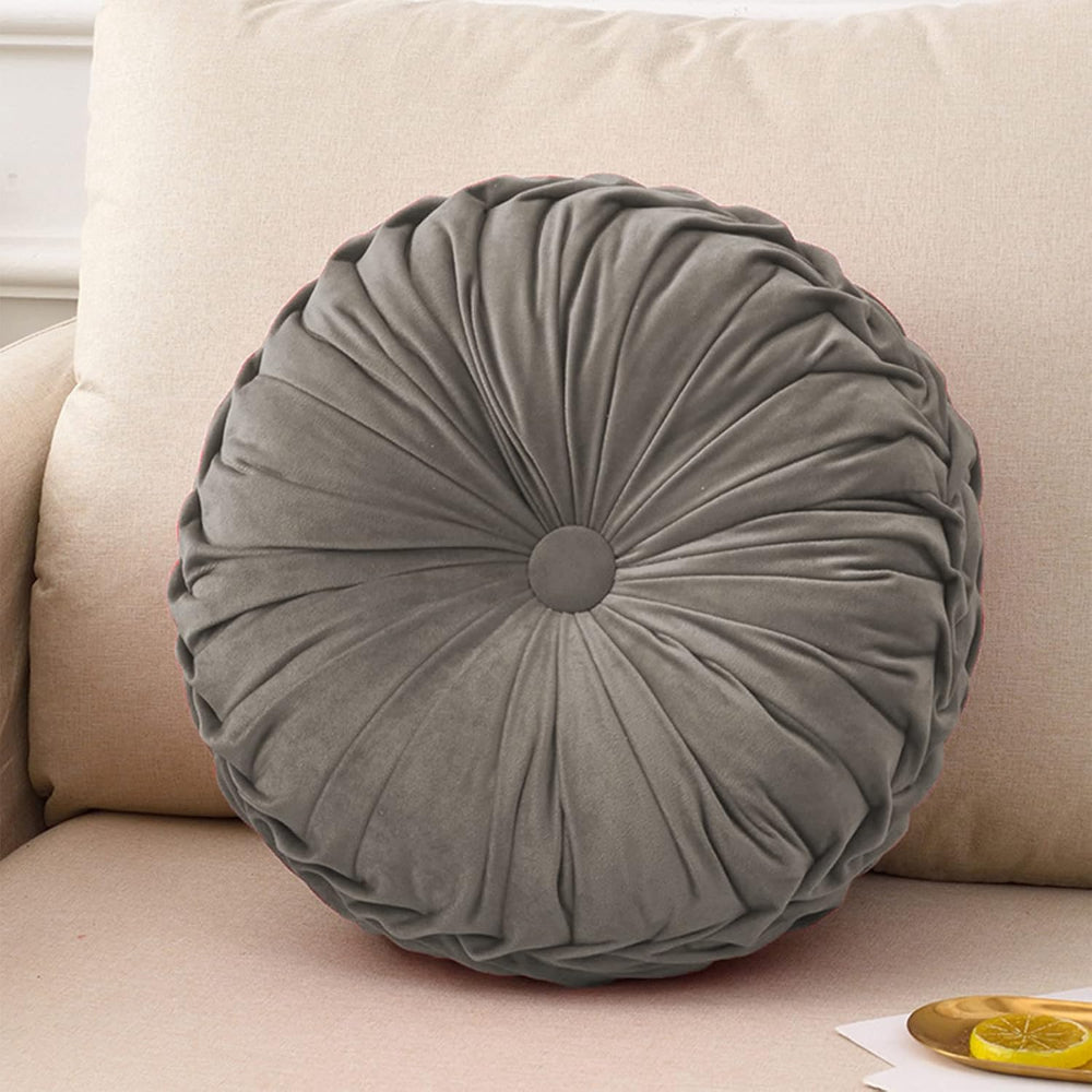 Round gray pillow on a beige sofa with a lemon on a coaster in the background.
