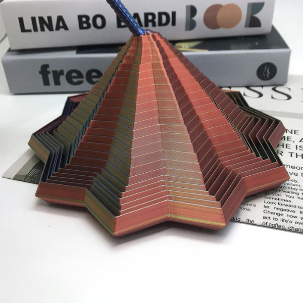 Colorful folded paper sculpture on a white surface with books in the background