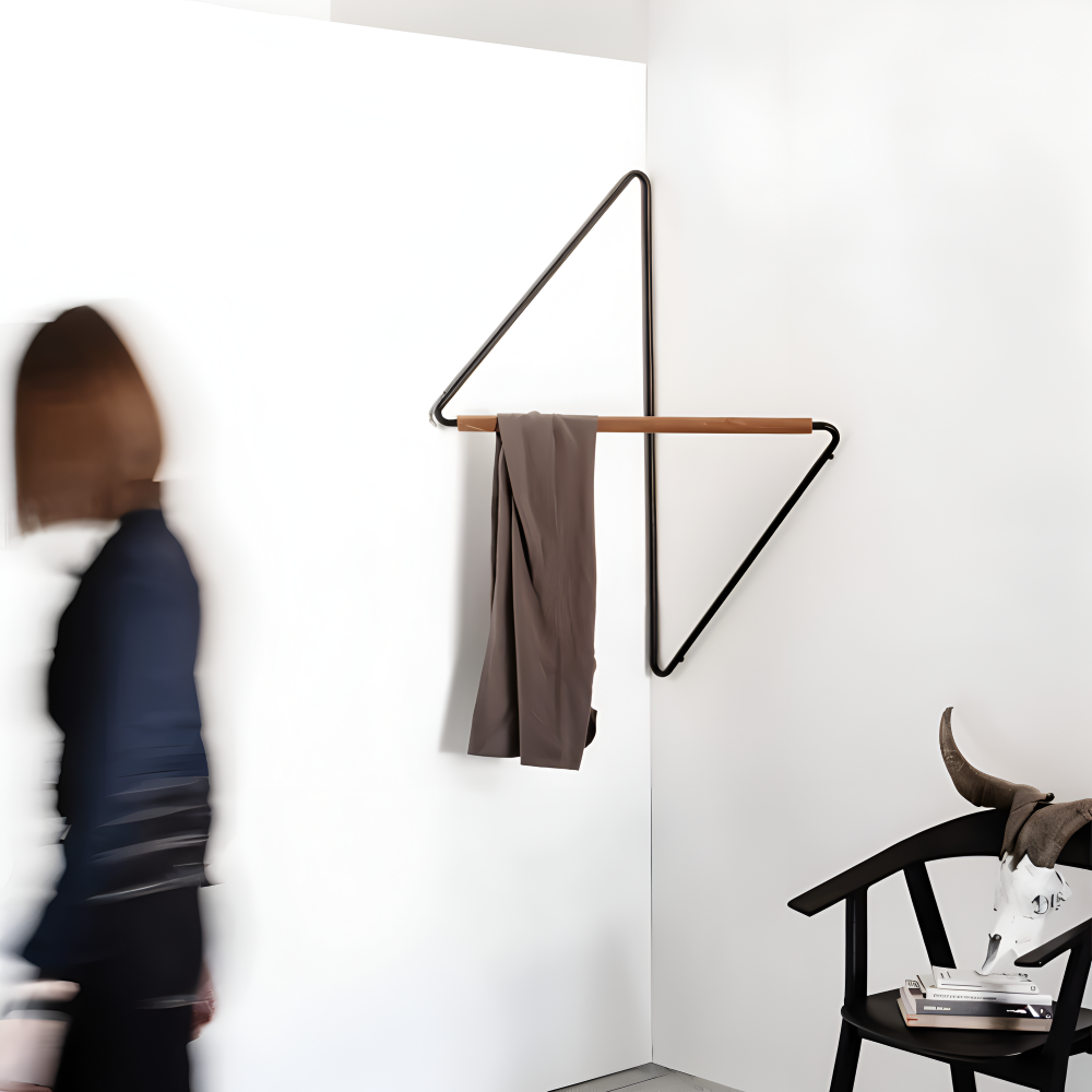 Modern wall-mounted coat rack with a brown garment on a white wall.