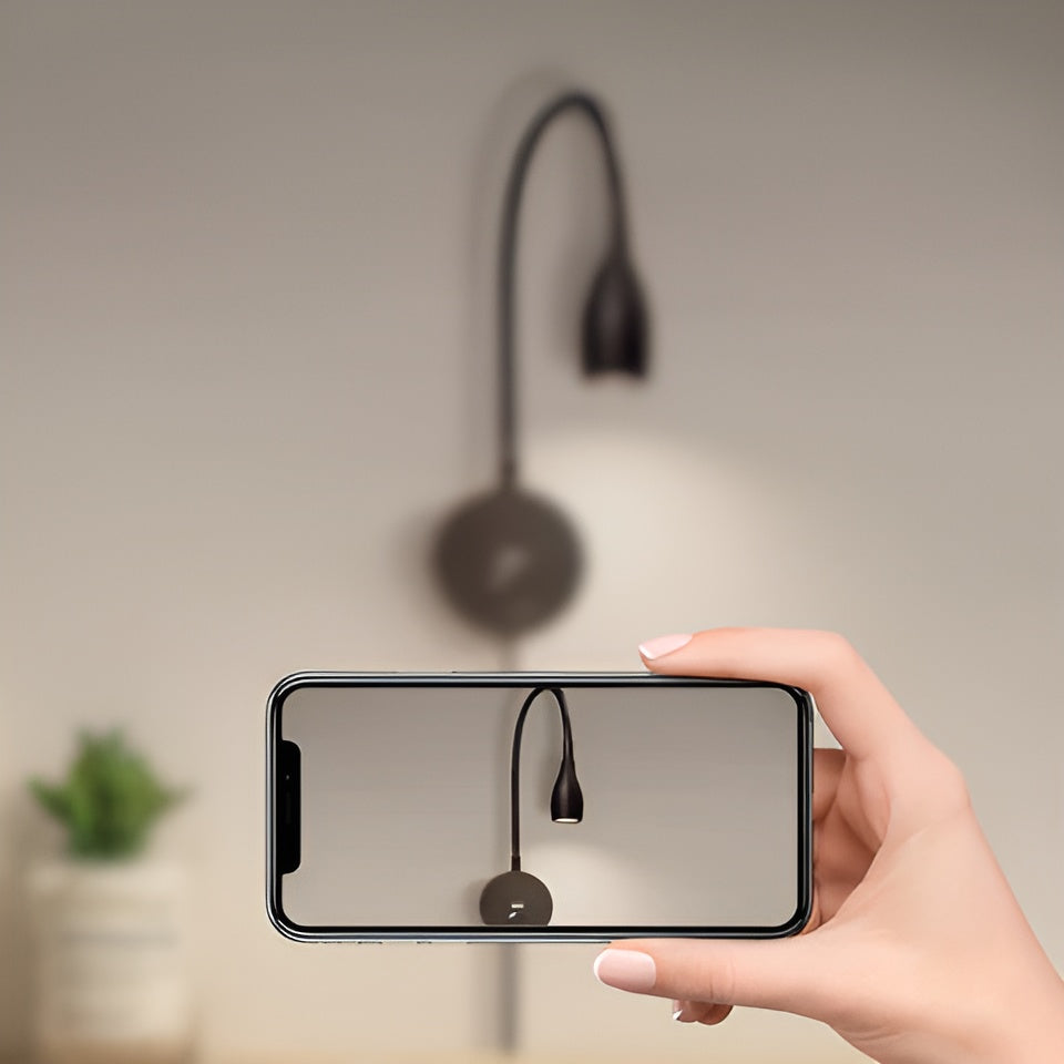 Hand holding a smartphone displaying an image of a wall-mounted lamp, with the actual lamp in the background.