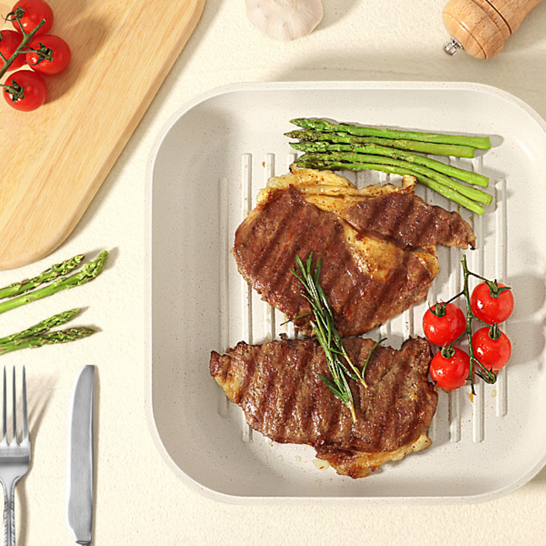 Grilled steaks on a white plate with asparagus and tomatoes, set on a light surface.