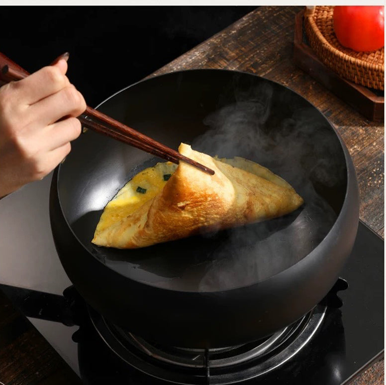 Person using chopsticks to fold an omelette in a hot pan on a stove.