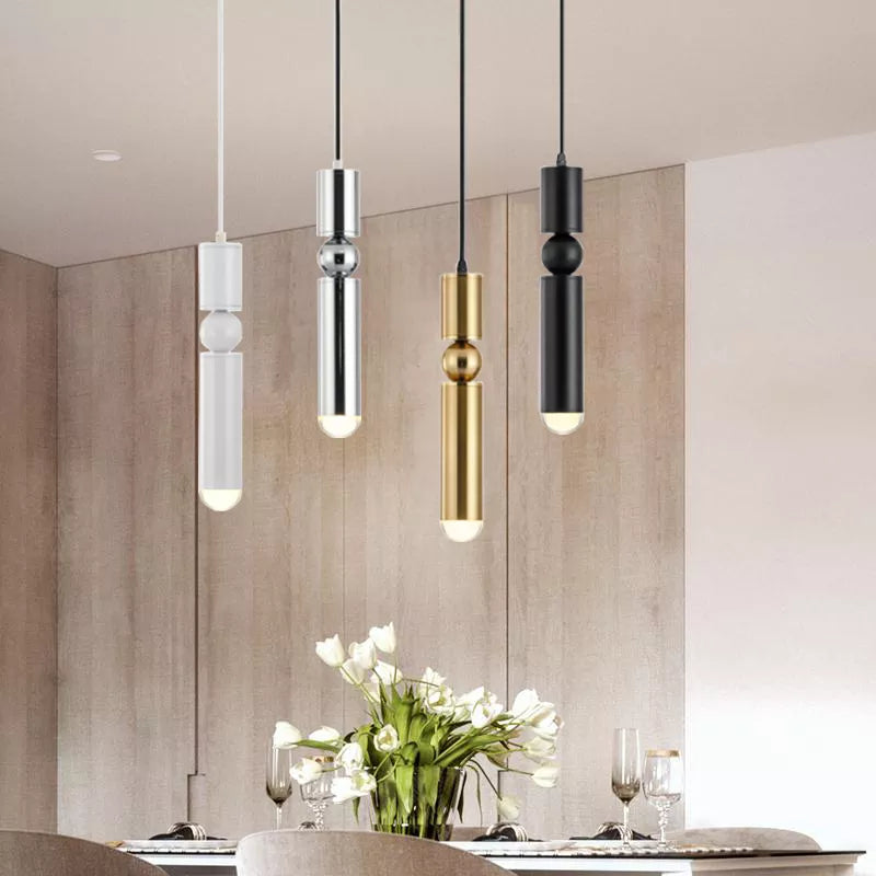 Modern pendant lights in white, silver, gold, and black hanging above a dining table with flowers.