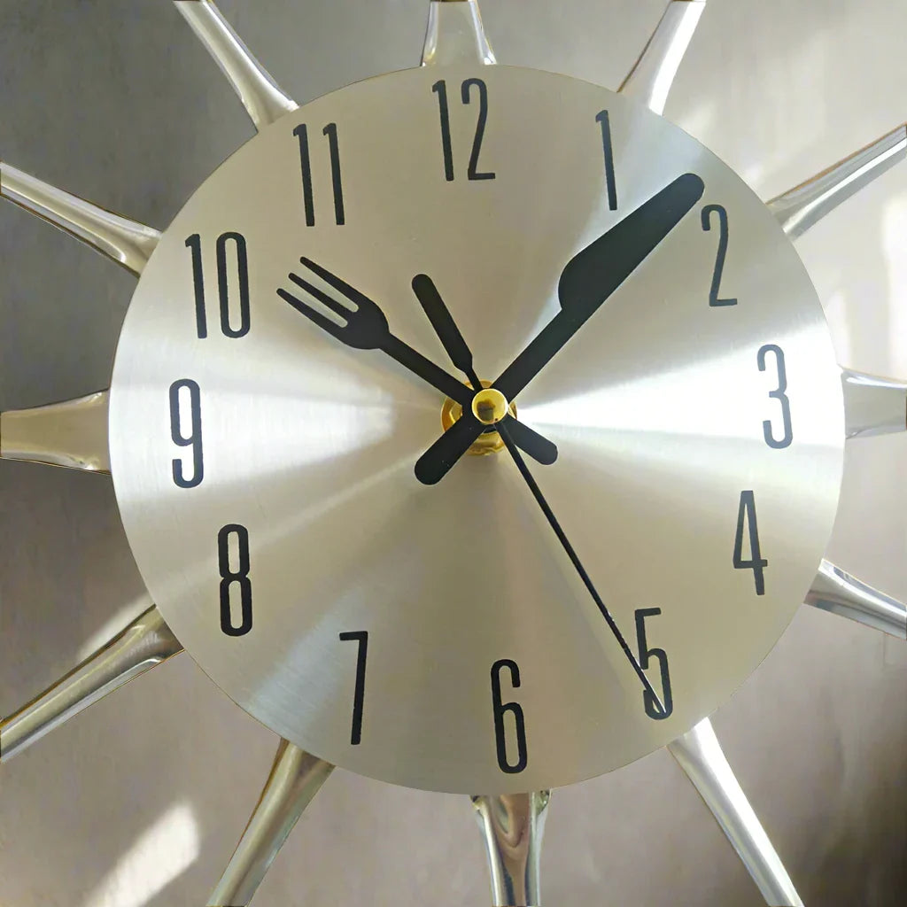 Clock with a fork and knife design on the hour markers against a neutral background
