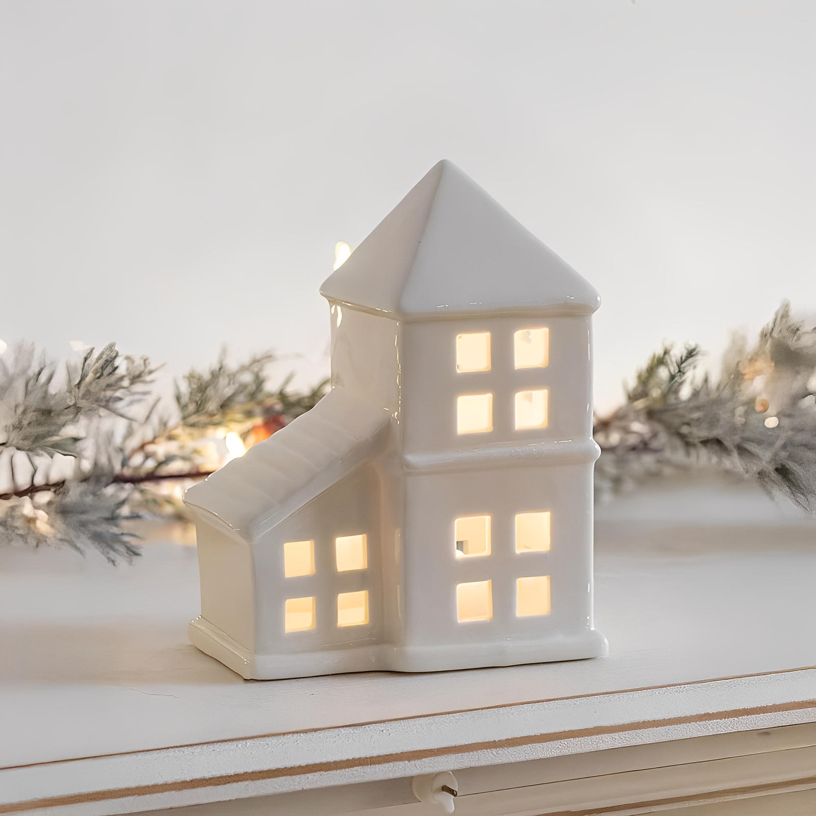 White ceramic house-shaped lantern with warm glow on a snowy surface
