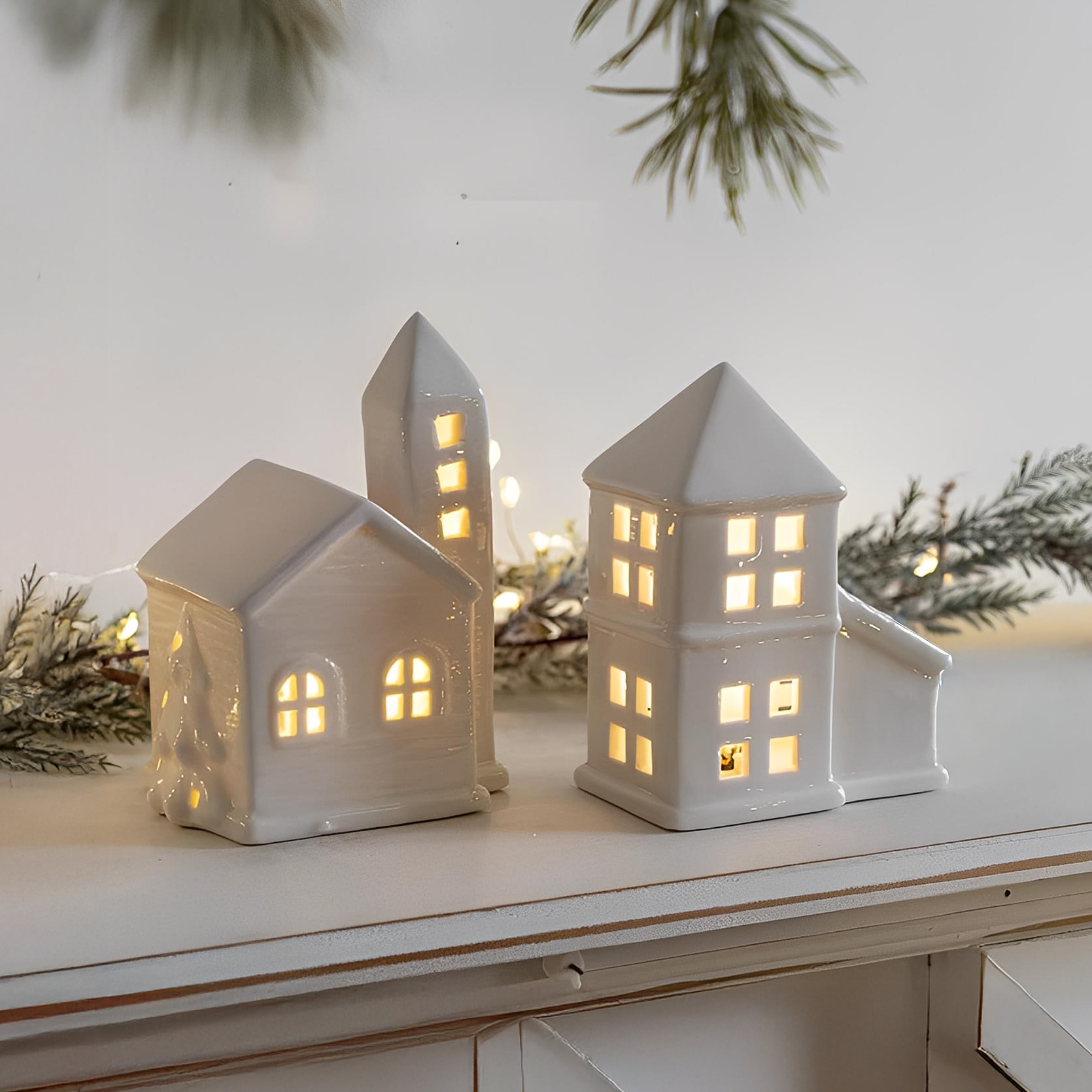 Two white ceramic house-shaped lanterns with glowing lights on a surface with a light background.
