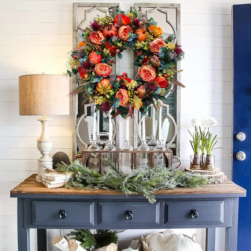 Decorative table with floral wreaths, plants, and a lamp against a white wall.