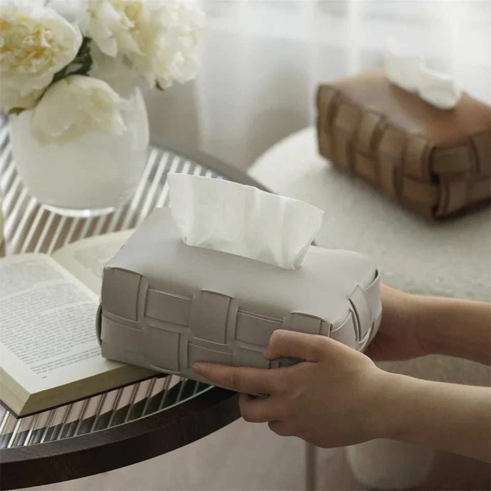 Person reaching for a tissue box on a table with a book and flowers in the background