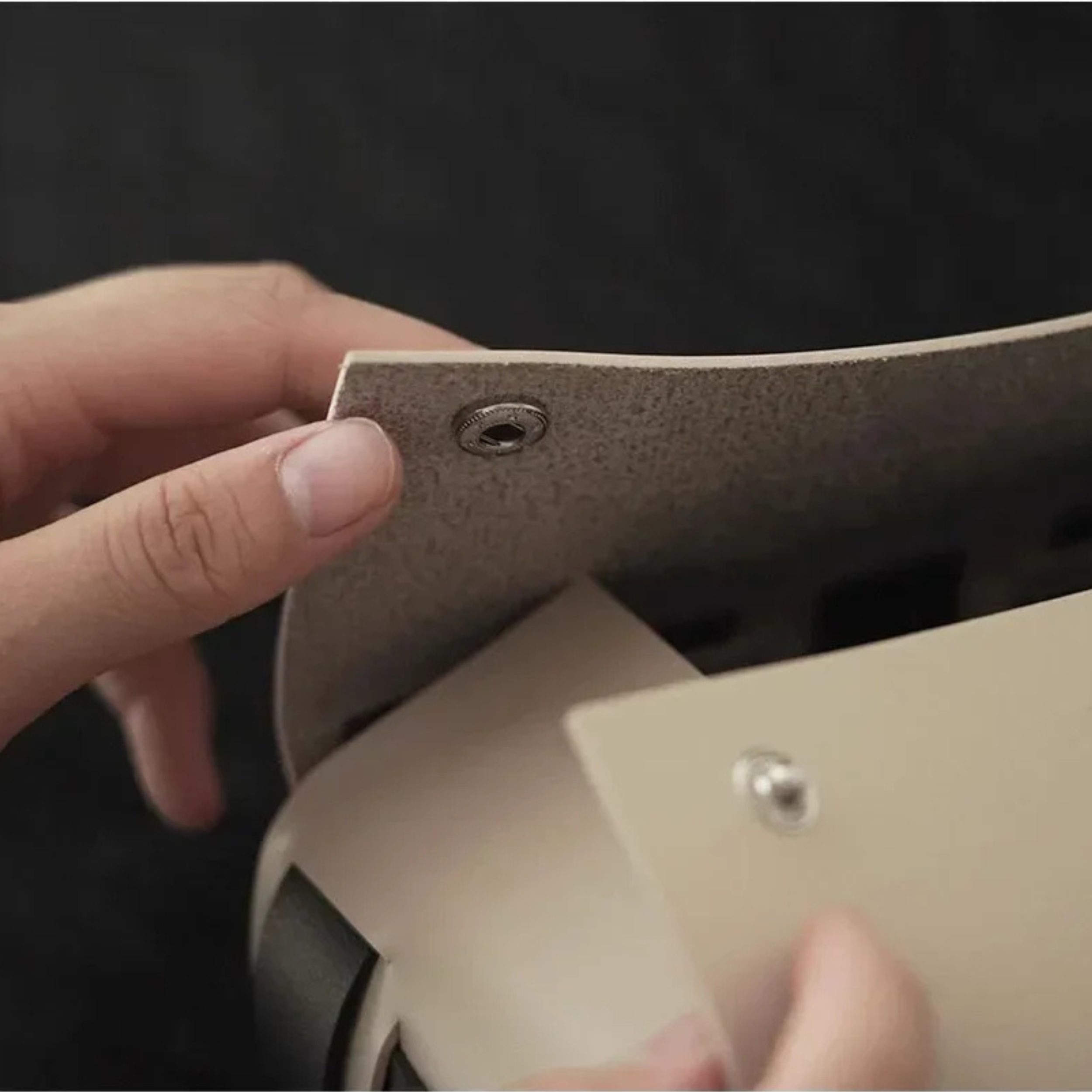 Close-up of a hand holding a beige leather wallet with a dark background