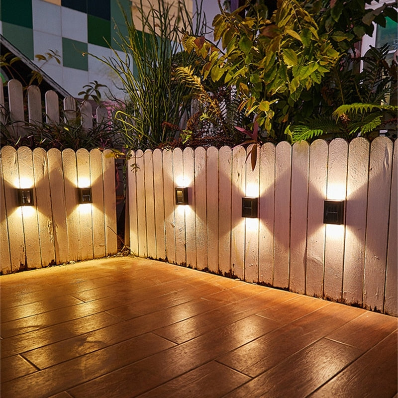 Wooden fence with wall-mounted lights casting a warm glow on a wooden deck.
