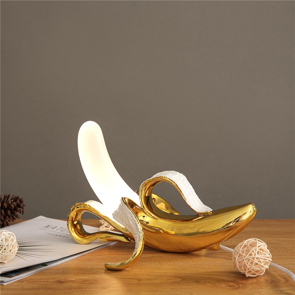 Decorative banana-shaped lamp with gold base on a wooden surface