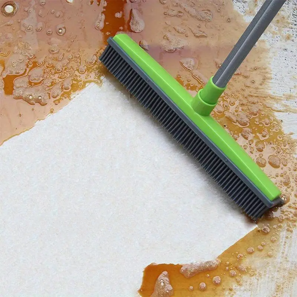Cleaning brush with green handle and black bristles on a wet surface with brown liquid.