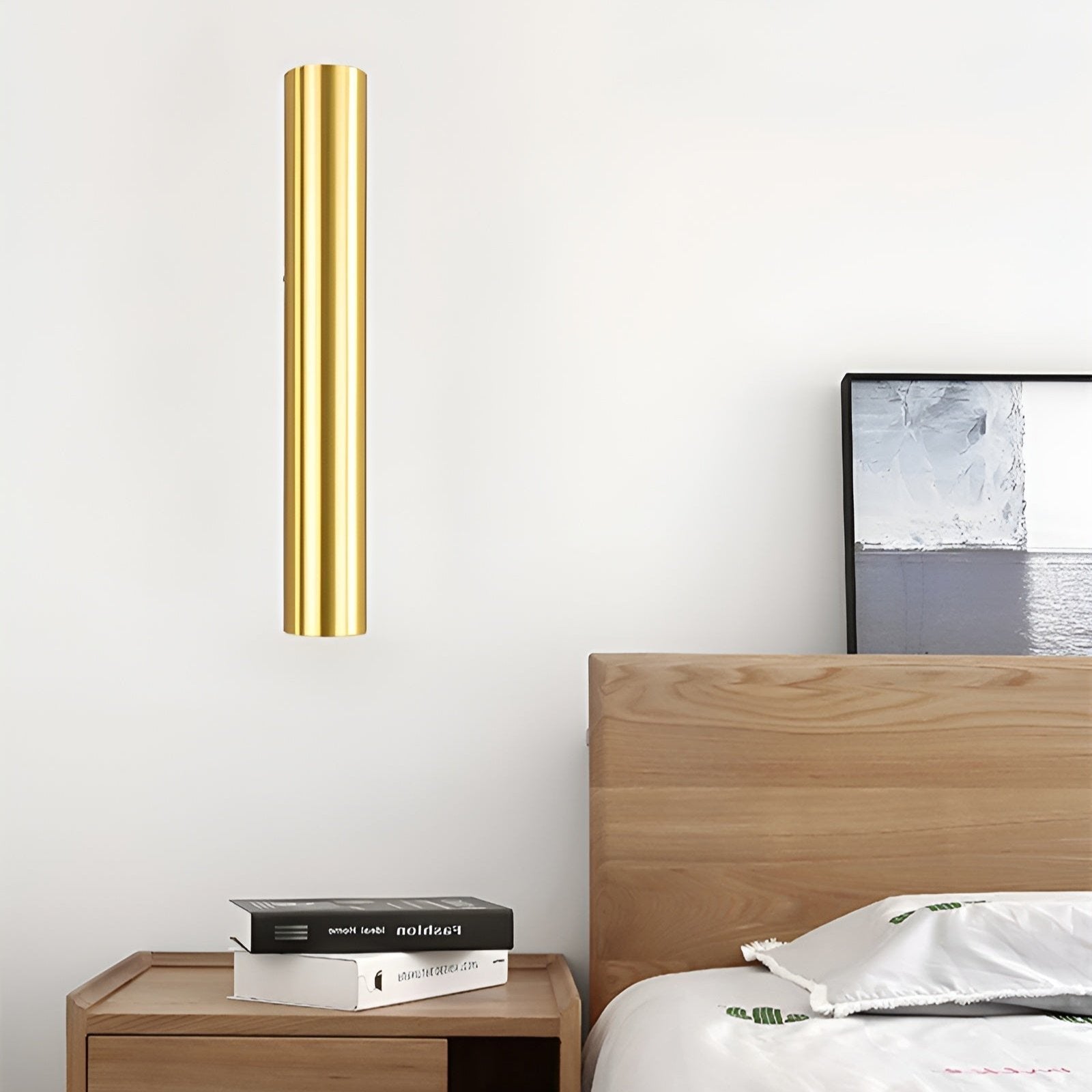 Gold cylindrical wall light fixture above a wooden nightstand with books and a wooden headboard.