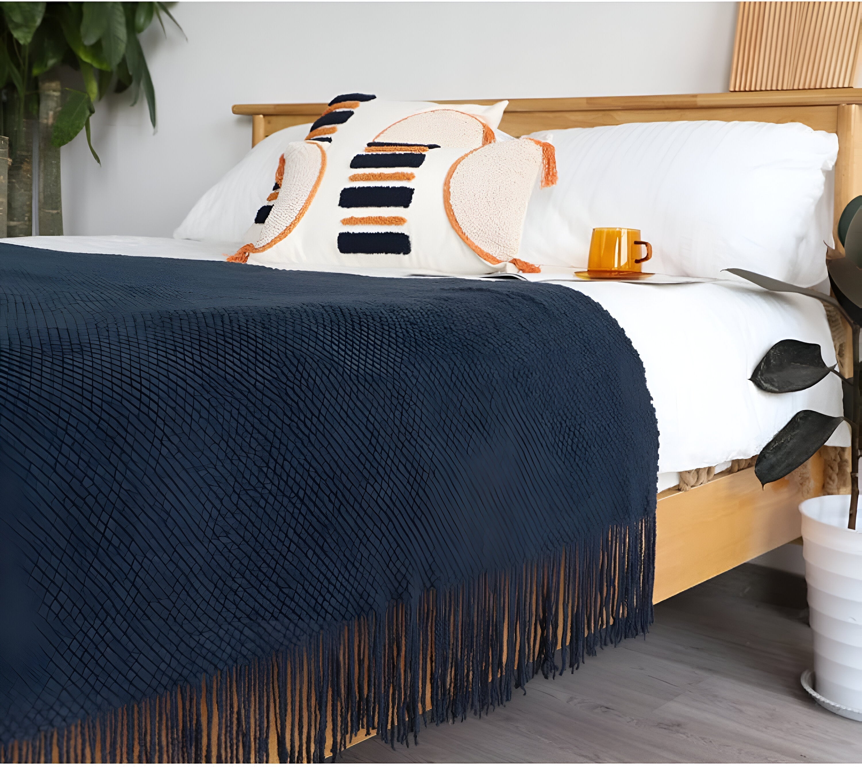 Navy blue blanket with fringe draped over a bed in a bedroom setting.