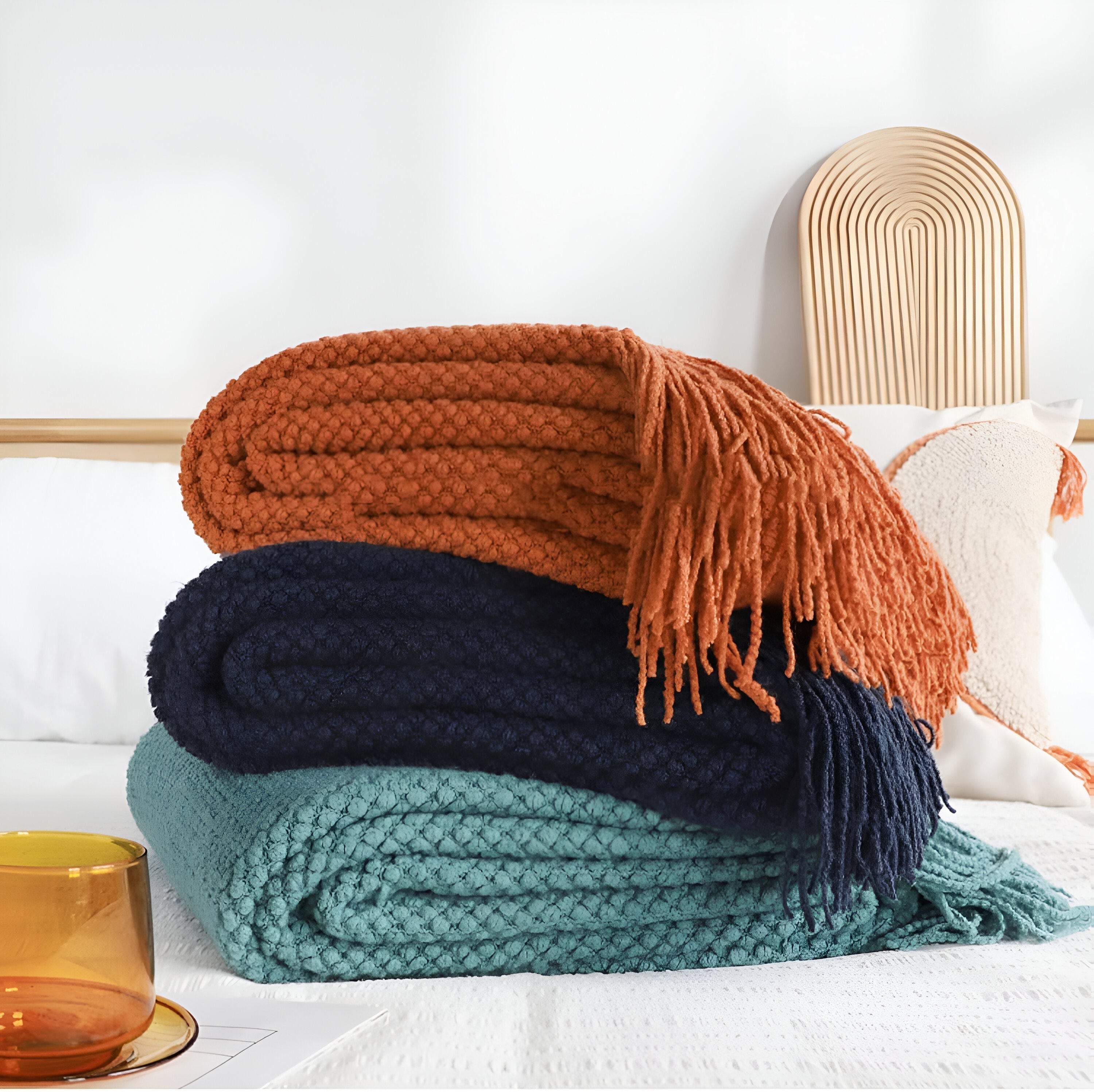 Stack of colorful knitted blankets on a bed with a white background