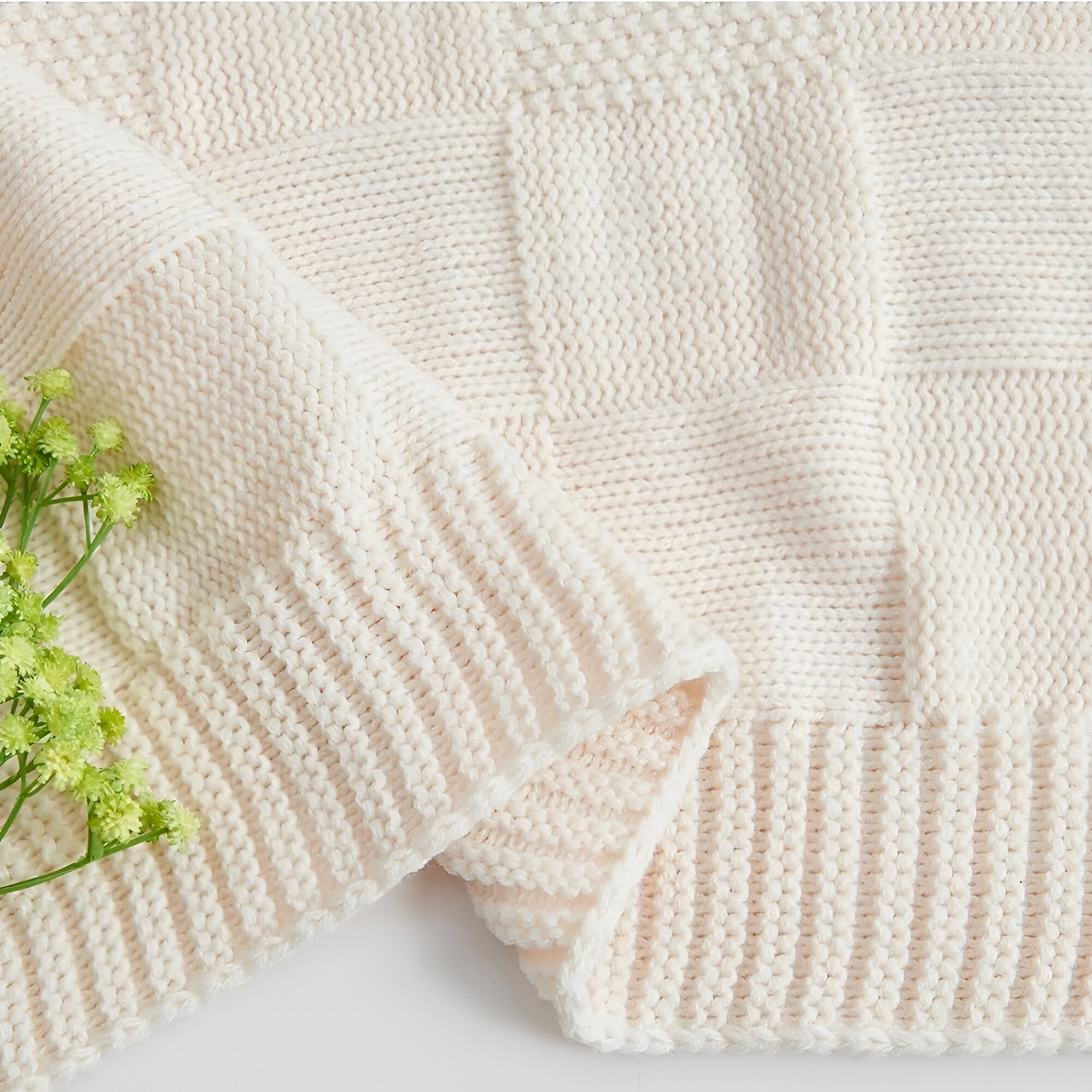 Close-up of a textured beige blanket with a corner folded over, on a light background.