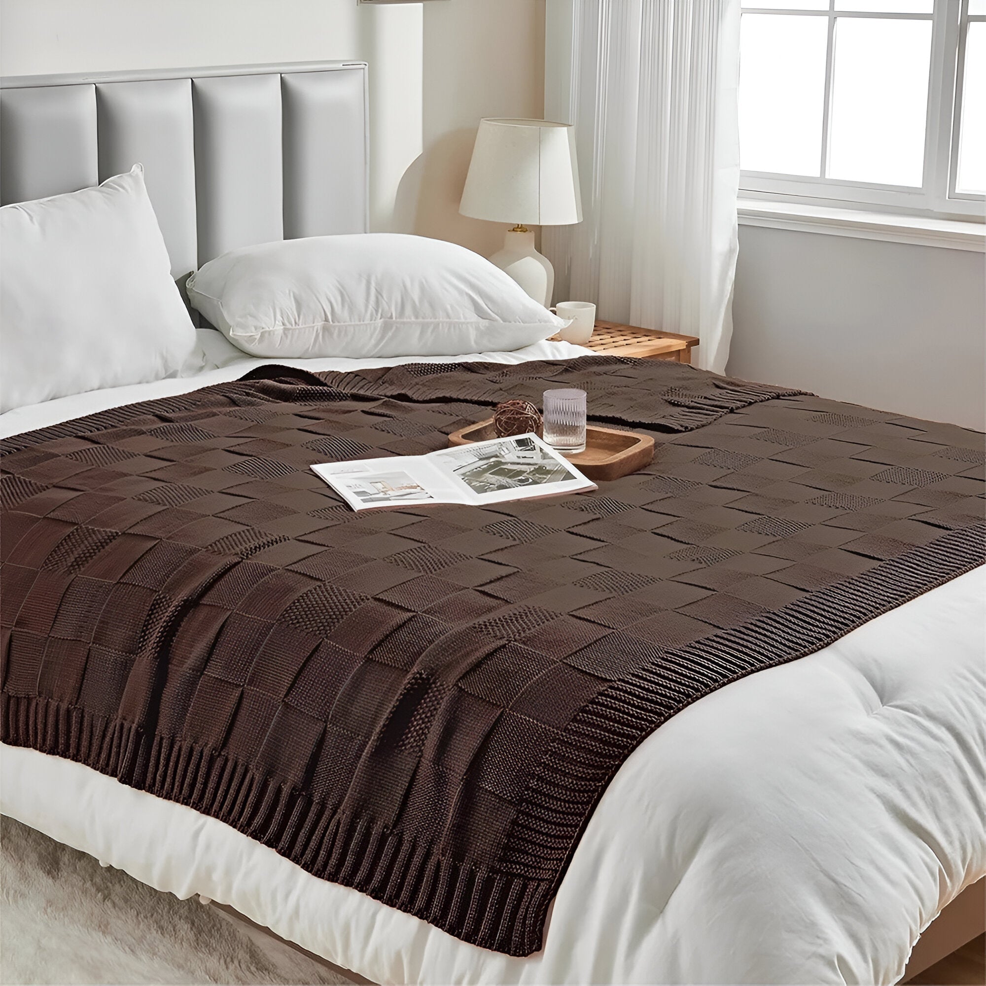Brown textured blanket on a bed with white pillows and a side table.