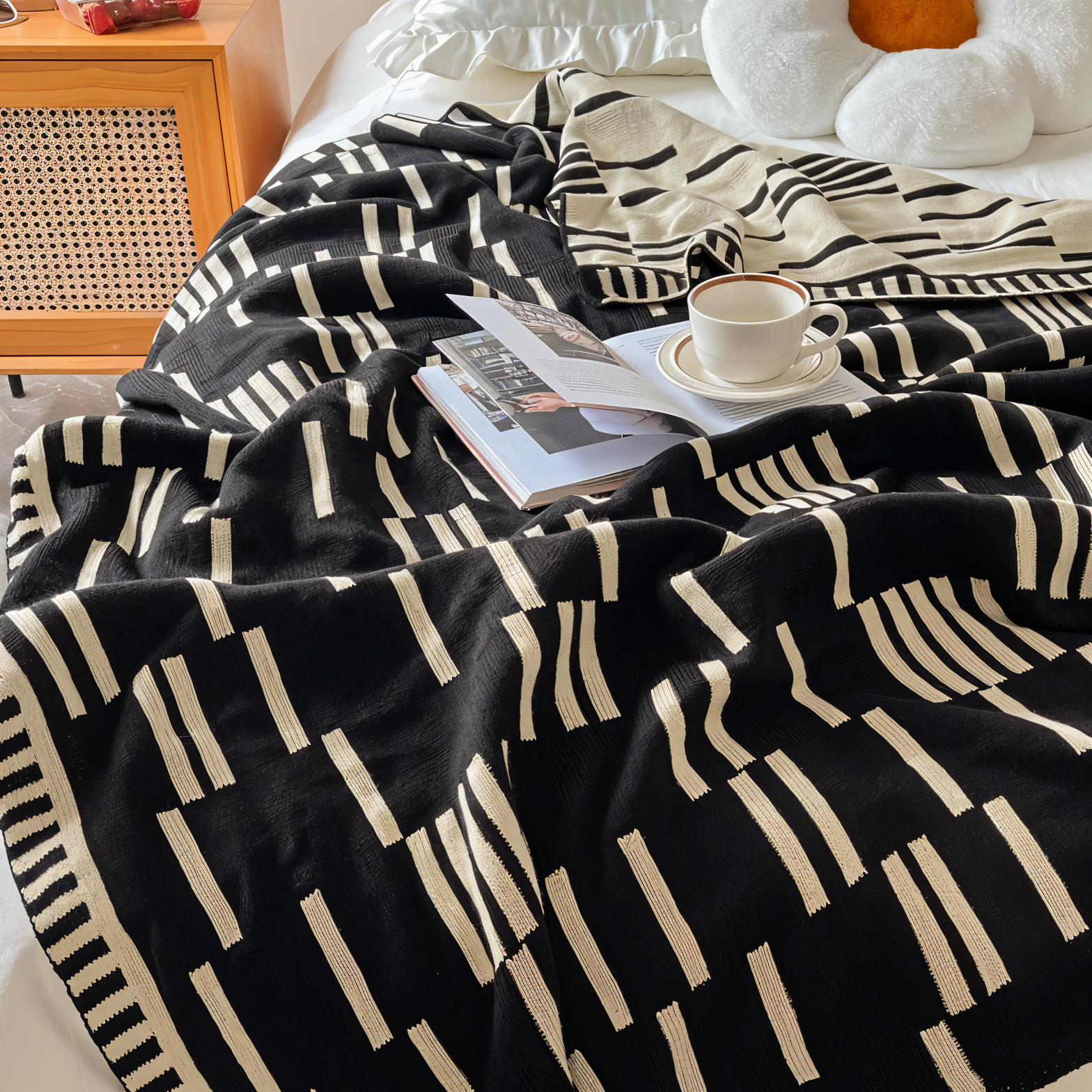 Black and white patterned blanket draped over a bed with a book and cup on top.