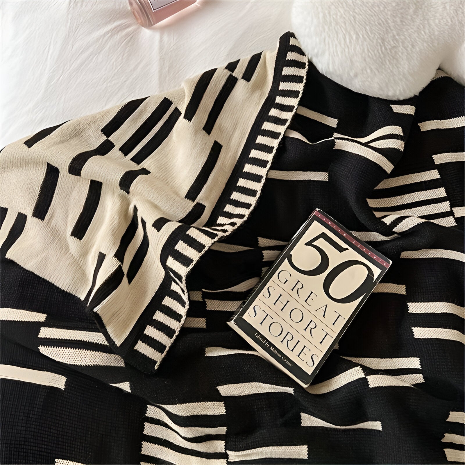 Black and white striped blanket with a book titled '50 Great Short Stories' on top