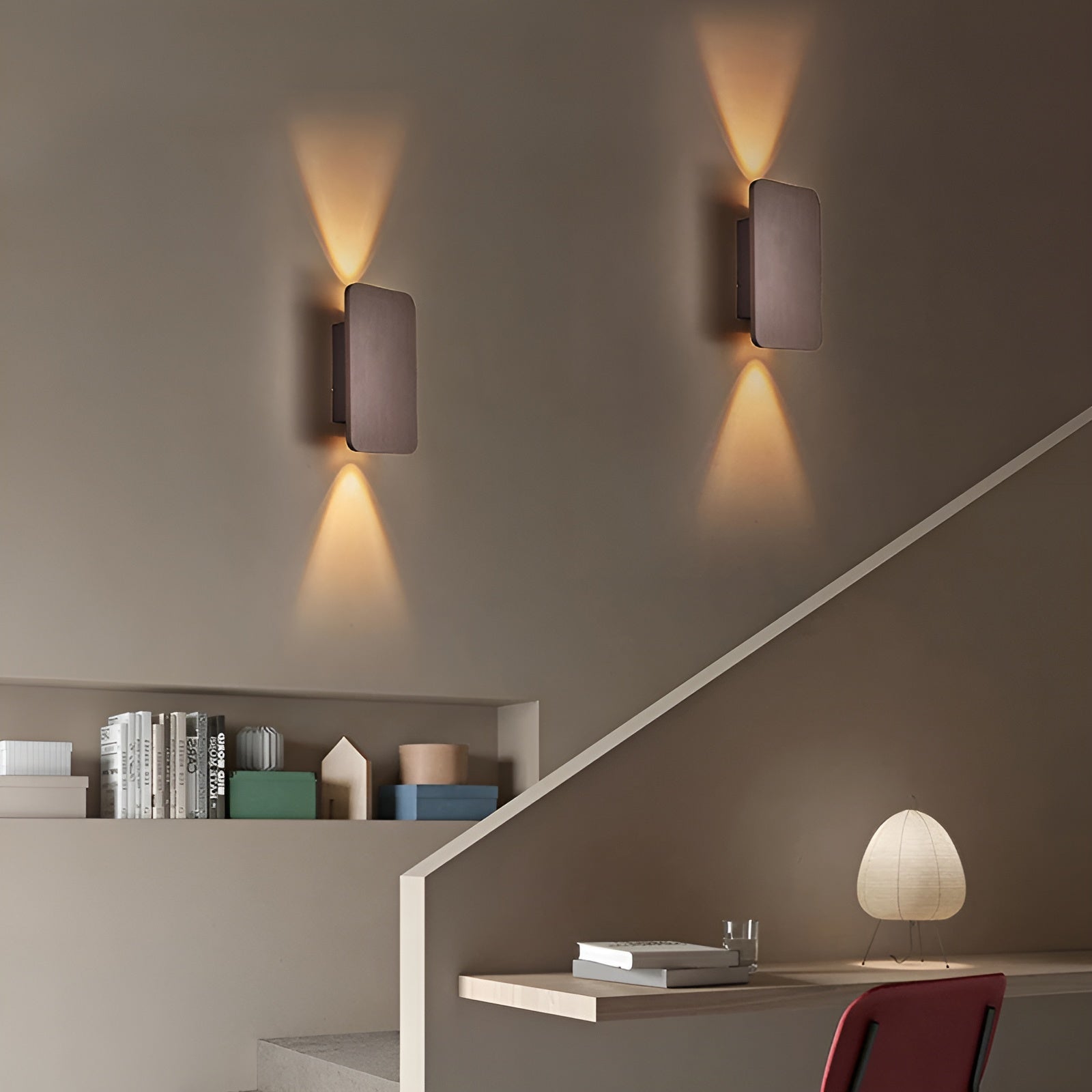 Modern wall lights on a gray wall with a staircase and decor items below.