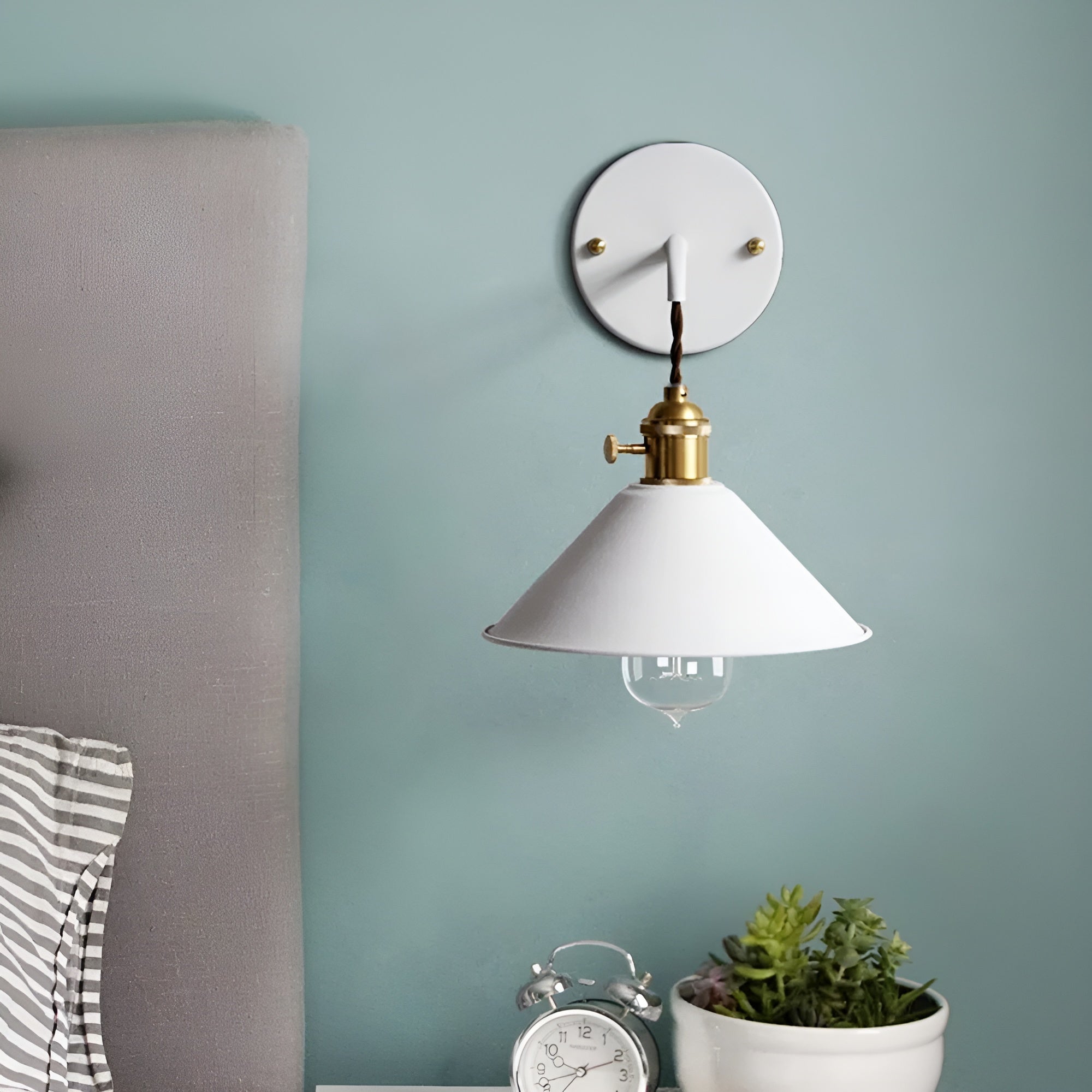 Wall-mounted lamp with white shade and gold accents on a light blue wall.
