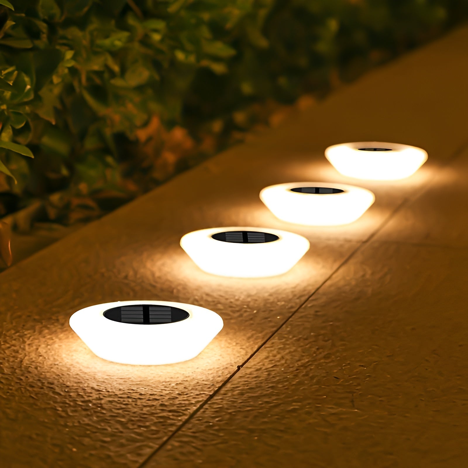 Four solar-powered outdoor lights on a concrete surface with greenery in the background.