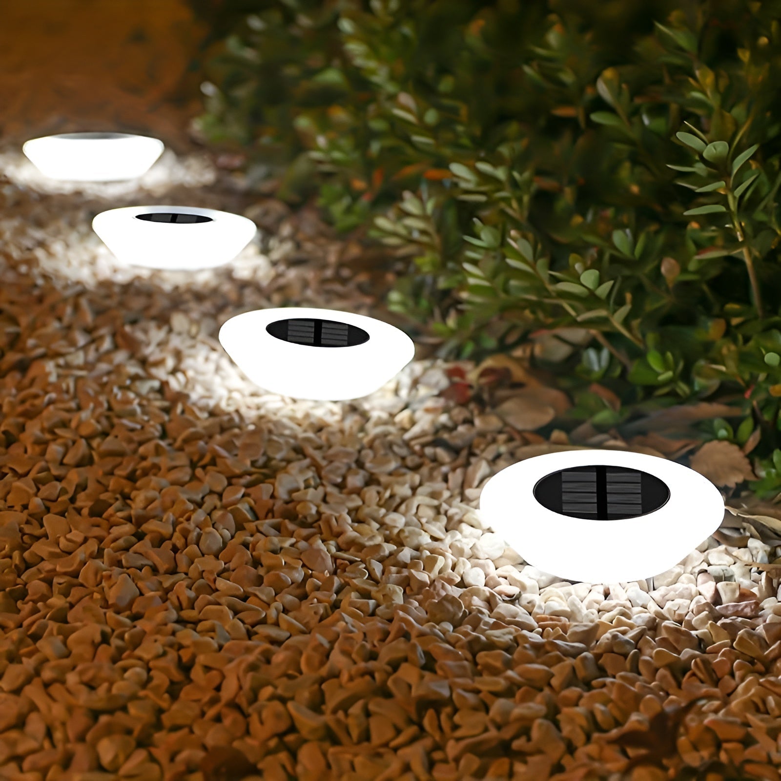Solar-powered outdoor lights embedded in a gravel pathway with greenery in the background.