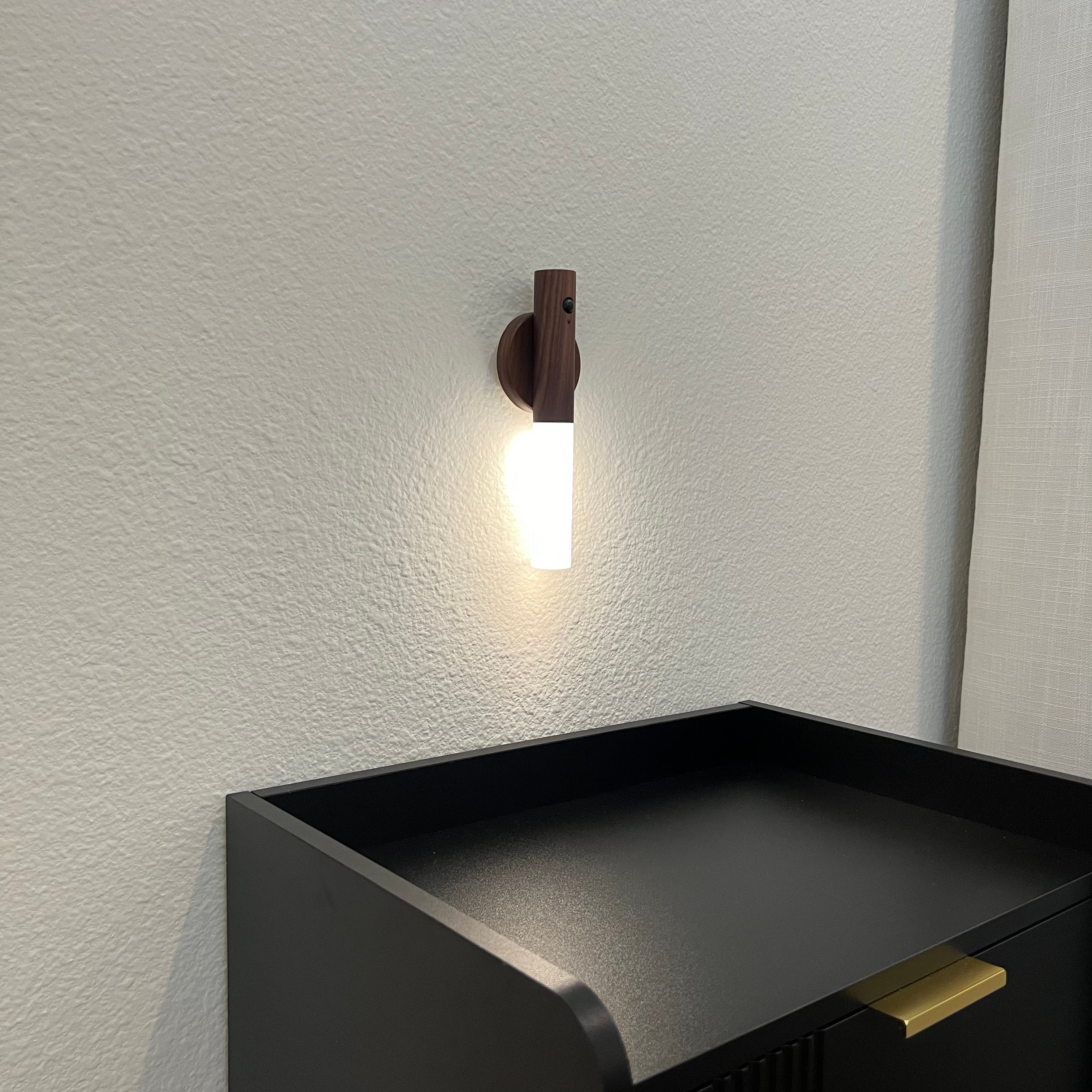 Wall-mounted light fixture on a textured wall above a black shelf.