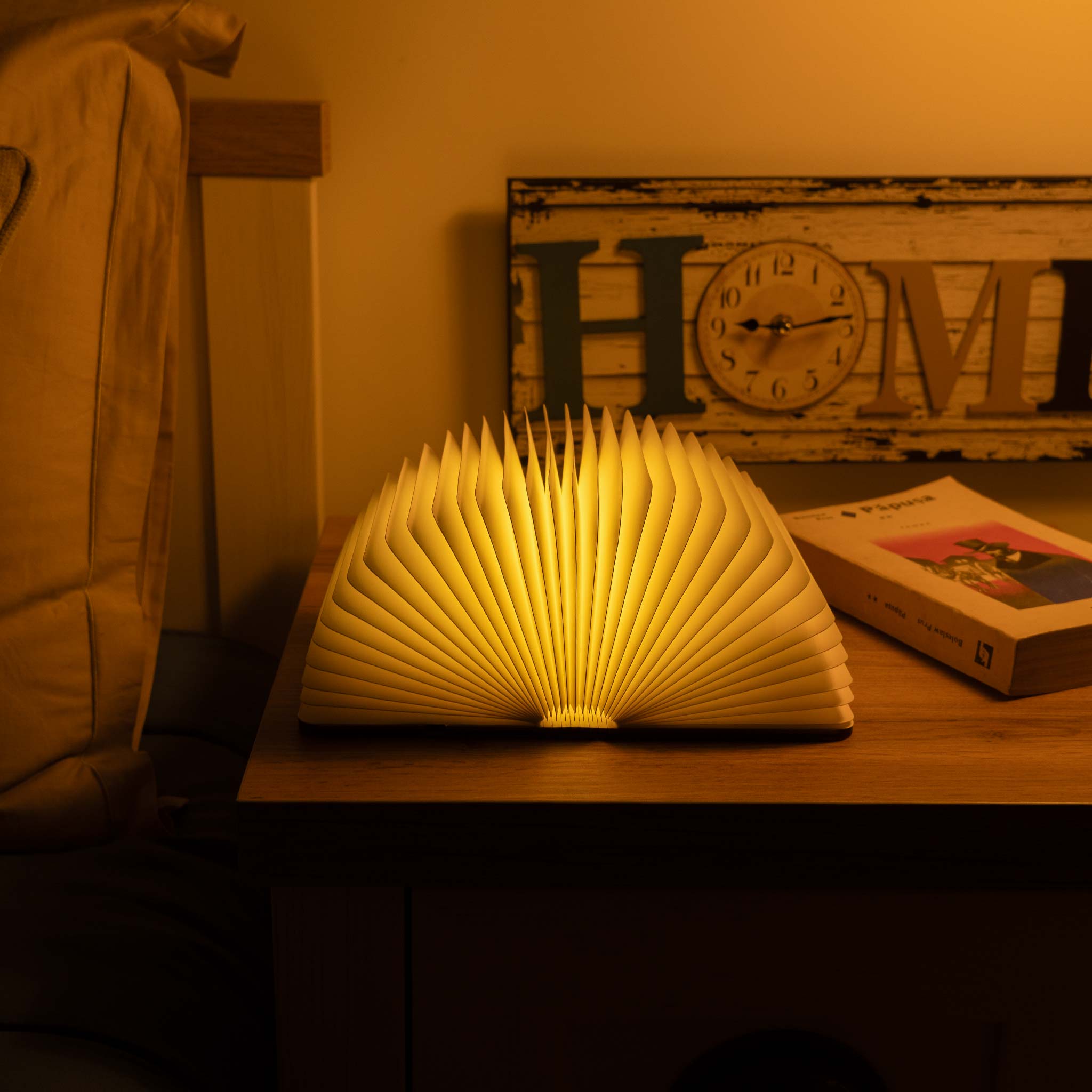 Book-shaped lamp on a wooden surface with a 'HOME' sign in the background