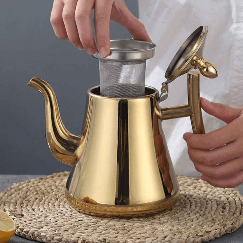 Gold teapot with a person removing a filter from it on a woven mat.