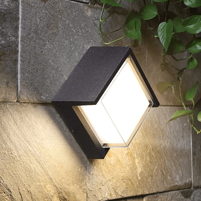 Outdoor wall light fixture on a stone wall with plants in the background