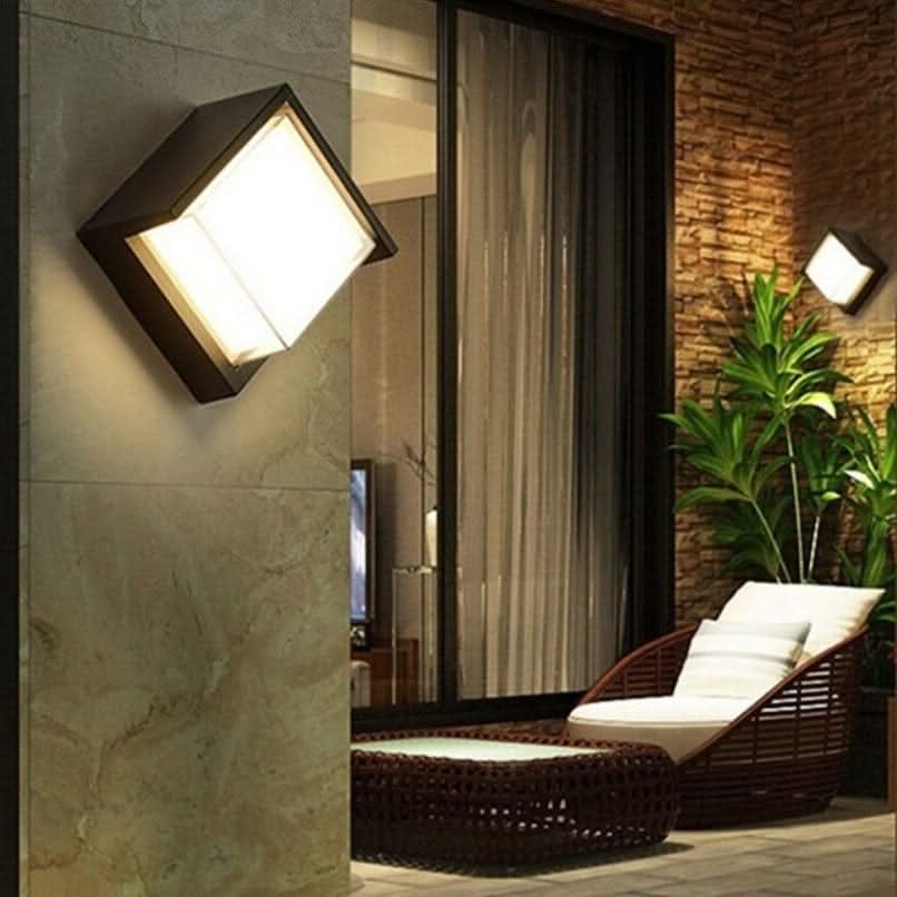 Modern outdoor wall light fixture on a stone wall with a lounge chair and plants in the background.