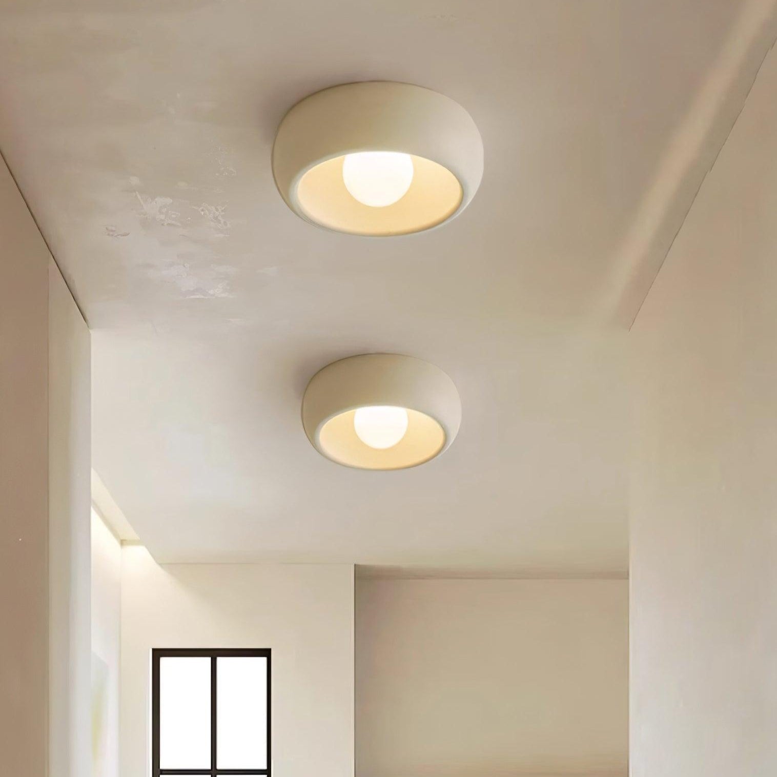 Two round ceiling lights on a white ceiling with a window and marble countertop in the background.