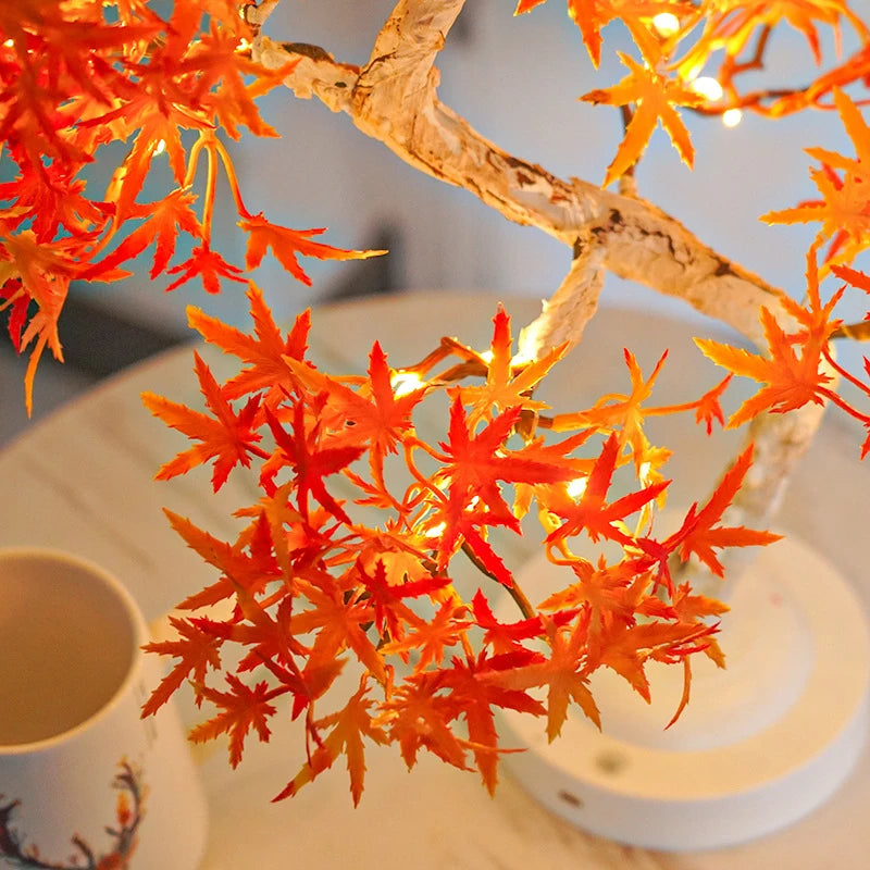 Artificial orange maple branches with lights on a white surface next to a cup.