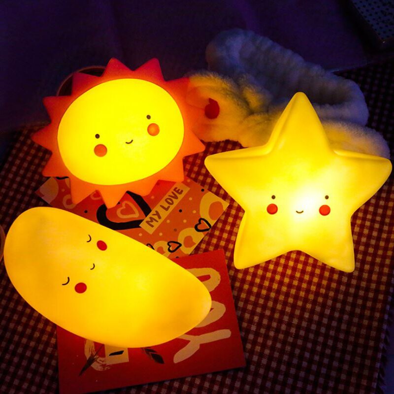 Three cartoonish night lights shaped like a sun, moon, and star on a checkered fabric background.