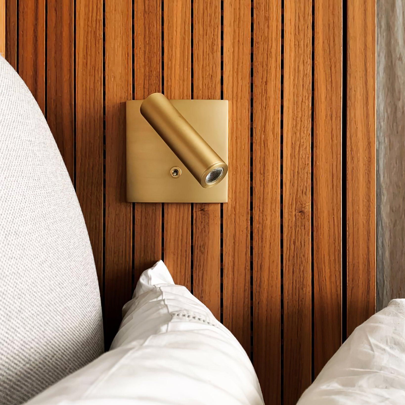 Gold wall-mounted light fixture on a wooden wall with white pillows.