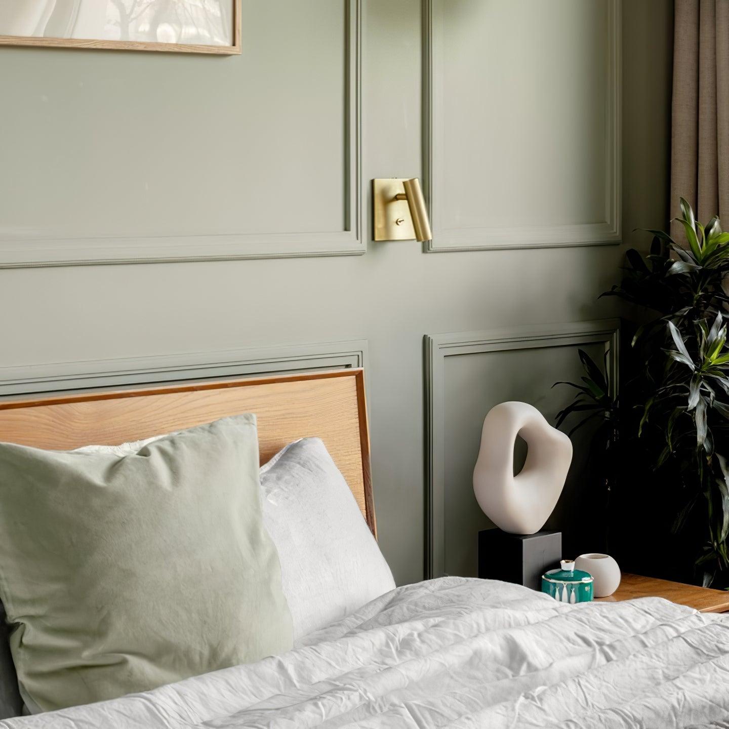 Neatly made bed with pillows, nightstand with decorative items, and wall art in a bedroom setting.