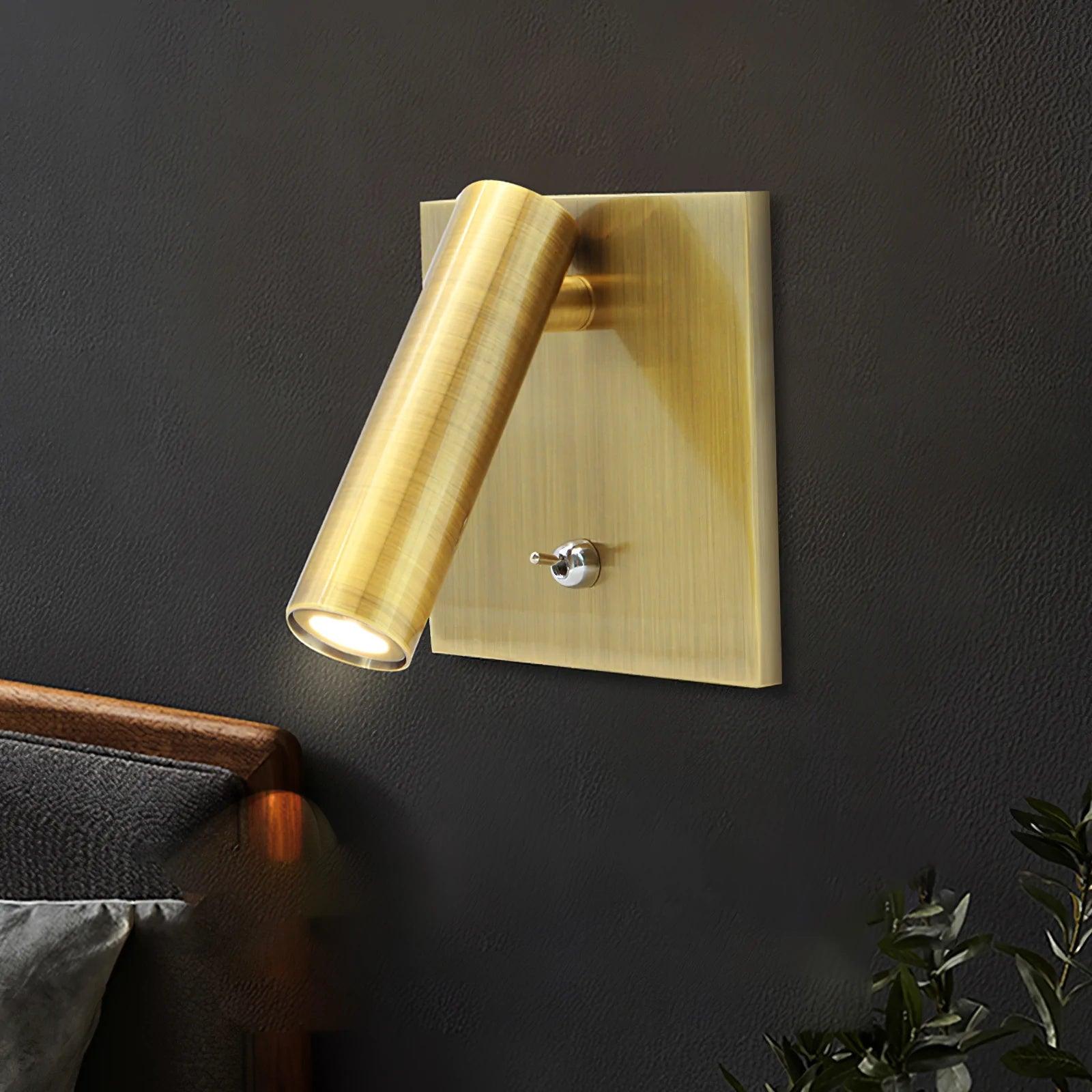 Gold wall sconce on a dark wall with a plant in the corner