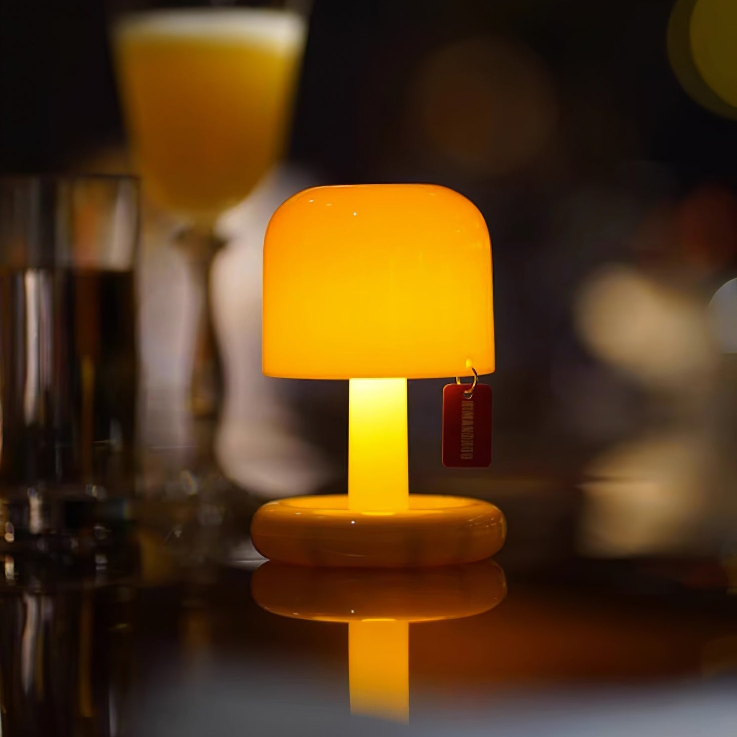 Small orange lamp on a reflective surface with blurred glasses in the background