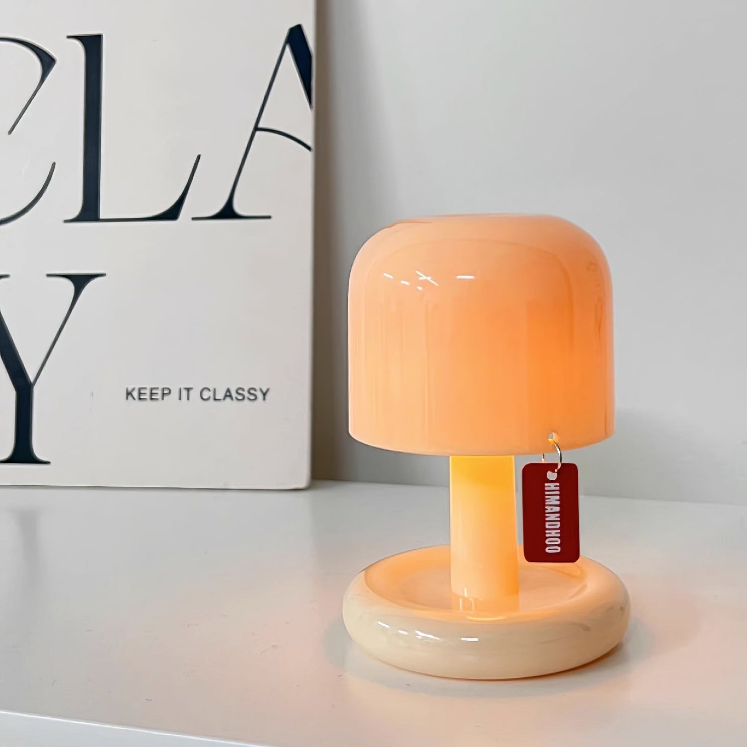 Small orange lamp with a tag on a white surface next to a book titled 'Keep It Classy'.